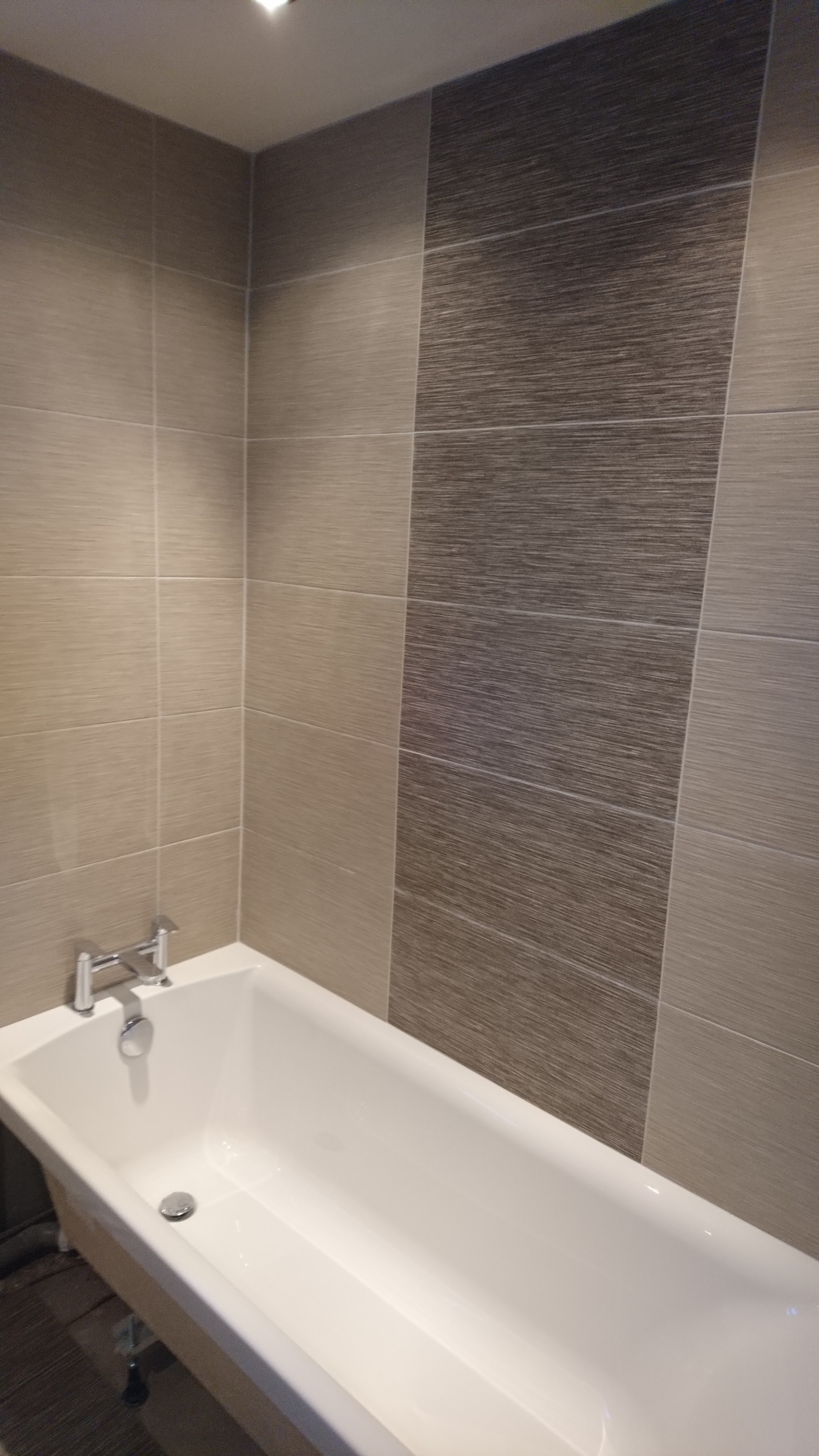 A tiled bathroom with a feature wall behind the bath